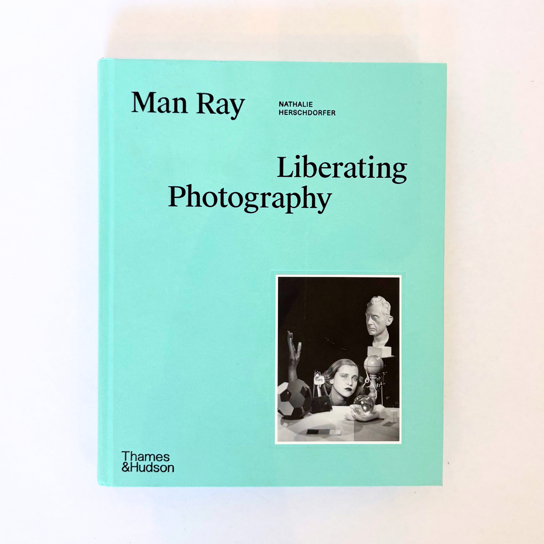 Book cover of 'Liberating Photography' by Man Ray with a light blue background and black text.